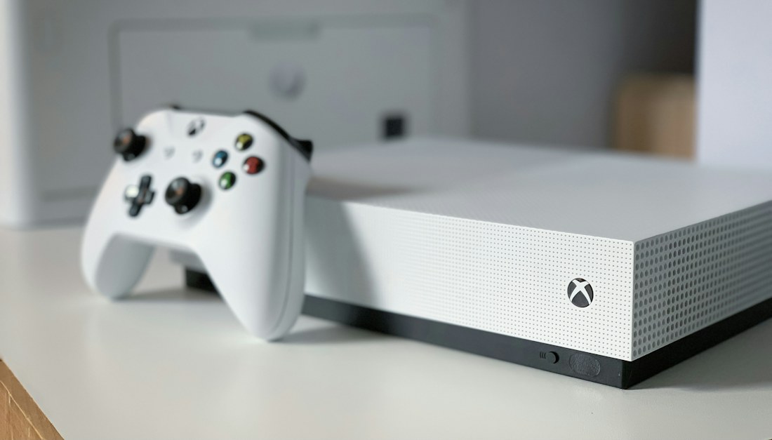 Consola de videojuegos blanca con su control inalámbrico sobre una mesa