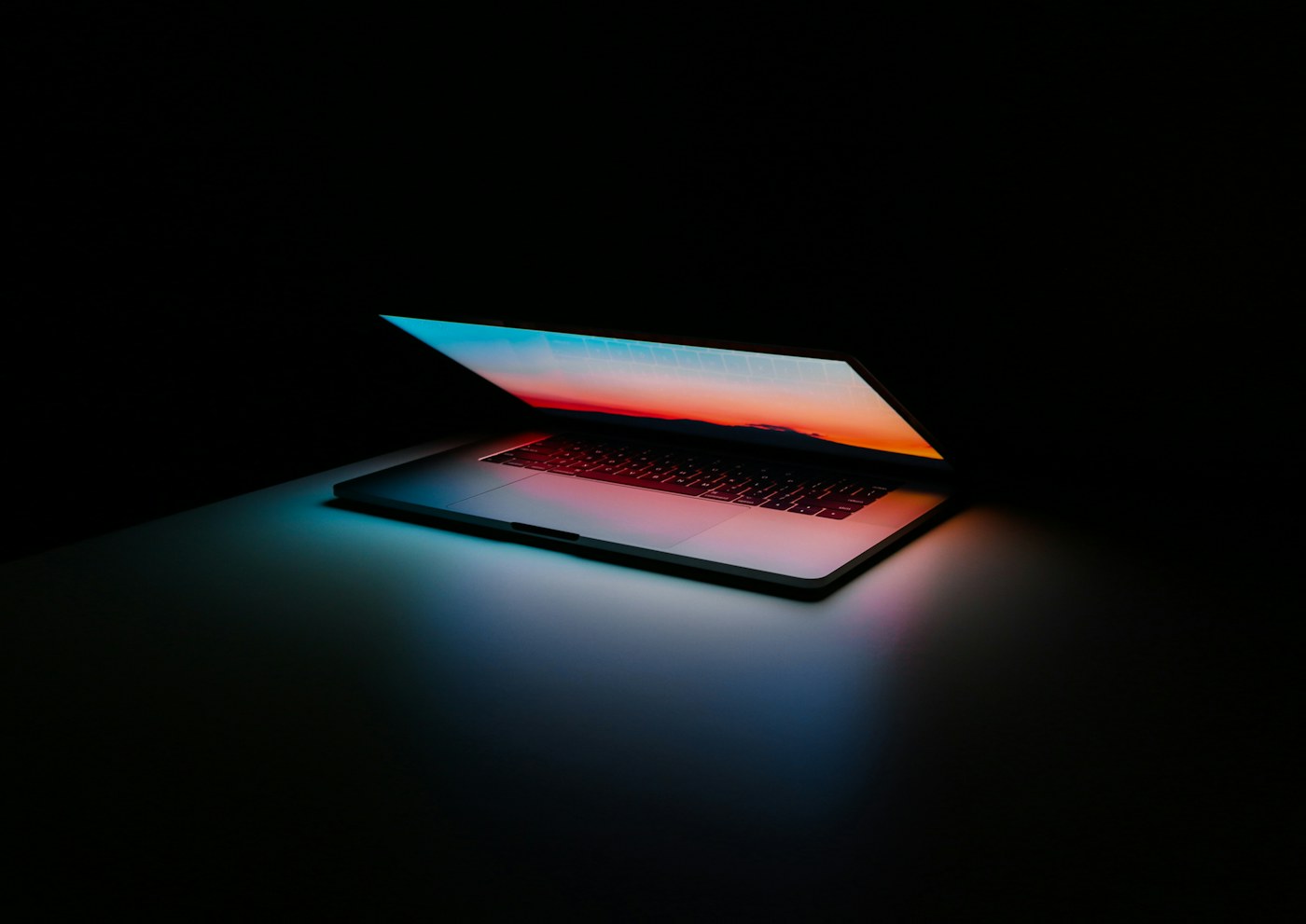 Laptop abierta en un escritorio oscuro con un resplandor rojo sobre el teclado